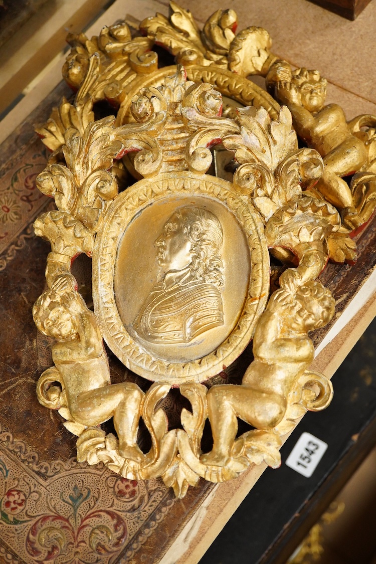 Two gilt metal plaques housed in giltwood ‘cherub’ frames and a heraldic leather folder with watered silk lining, 34 x 27cm